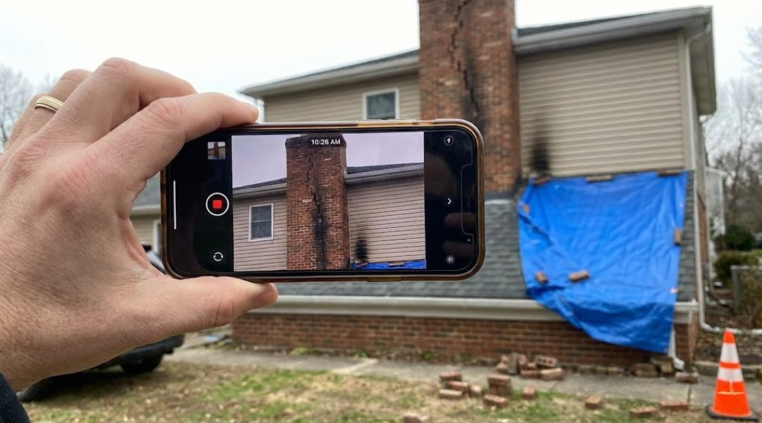 Homeowner filming a chimney damage video walkthrough for an insurance claim.